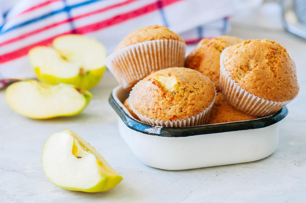 a few apple oatmeal muffins in a lunchbox, next to them small cut apples