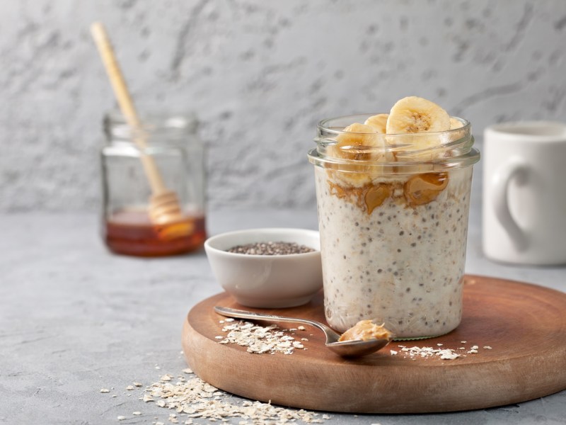 A glass of peanut butter overnight oats. In the background is a glass of honey.