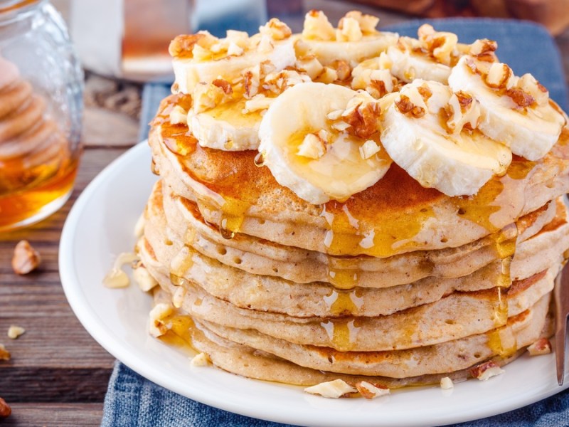 Pancakes on a white plate with banana, walnuts and syrup
