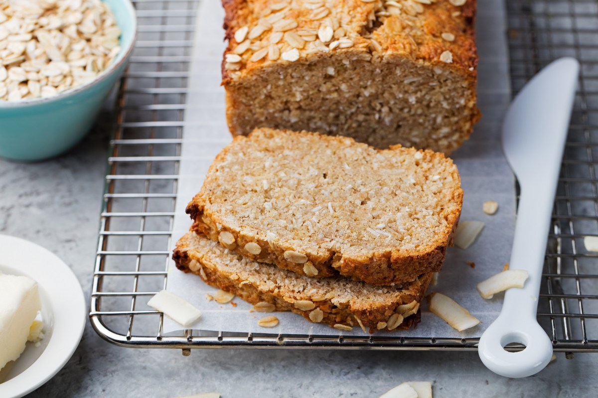 Sliced oatmeal quark bread on a board, next to it a bowl of oatmeal and a knife.
