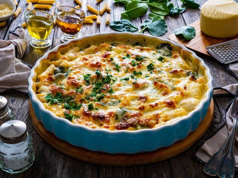 A round baking dish with pasta bake with feta and spinach, topped with cheese and sprinkled with parsley.