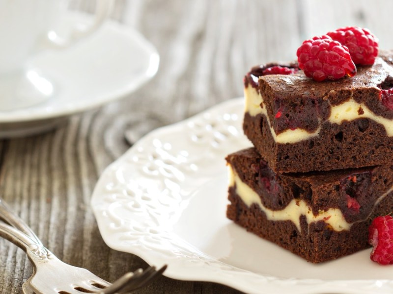 Two raspberry cheesecake brownies stacked on a plate.
