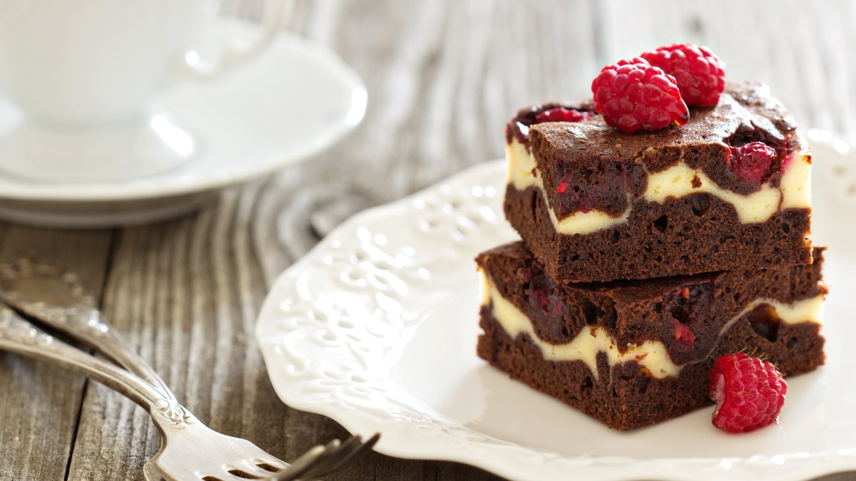 Two raspberry cheesecake brownies stacked on a plate.