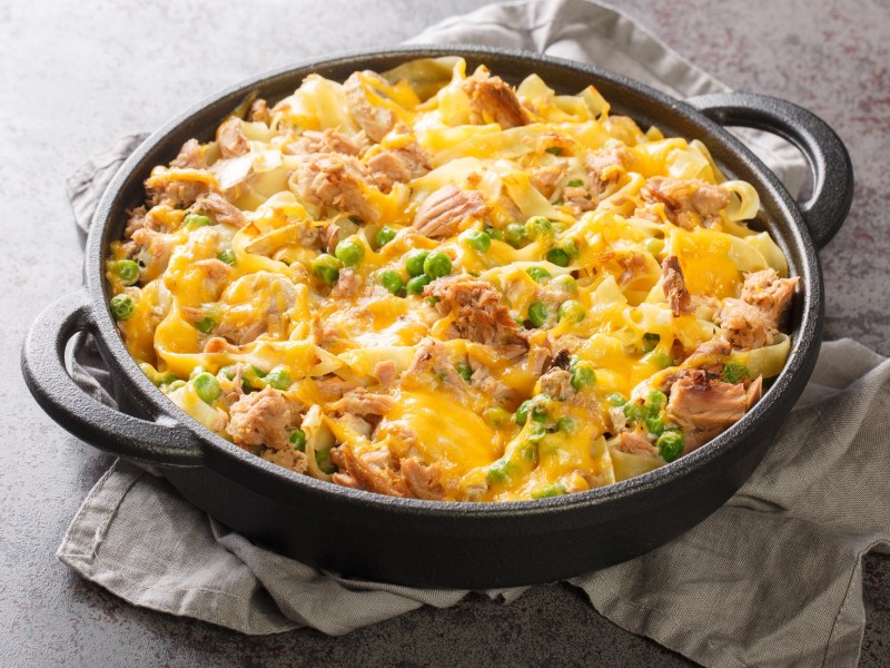 Tuna noodle casserole with peas in a cast iron baking dish on a gray cloth.