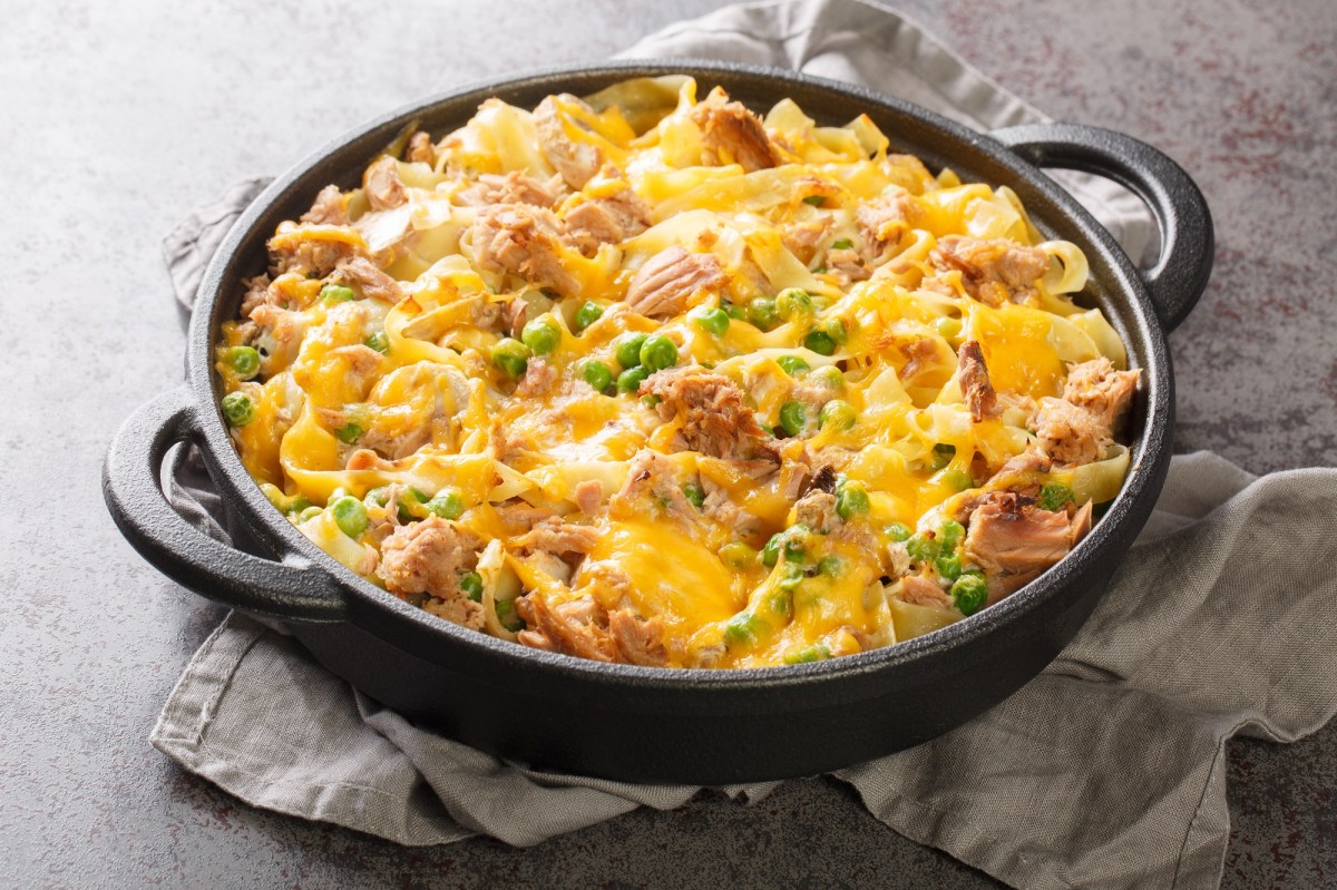 Tuna noodle casserole with peas in a cast iron baking dish on a gray cloth.