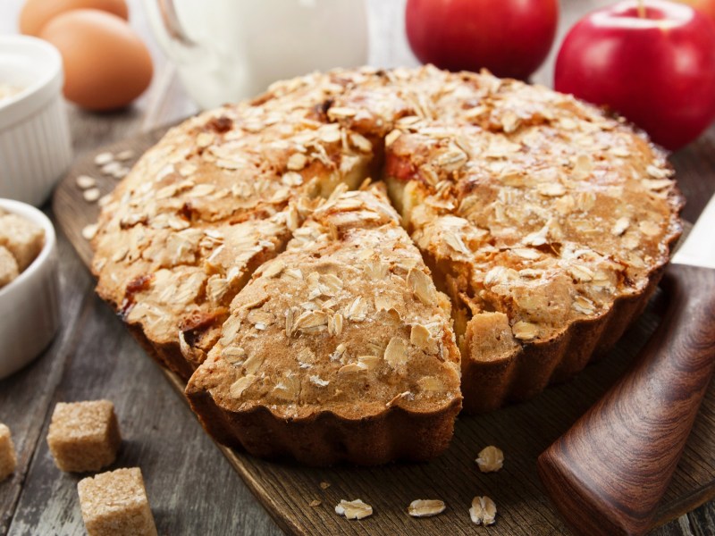Baking pan with apple-oatmeal cake on a table with apples next to it.