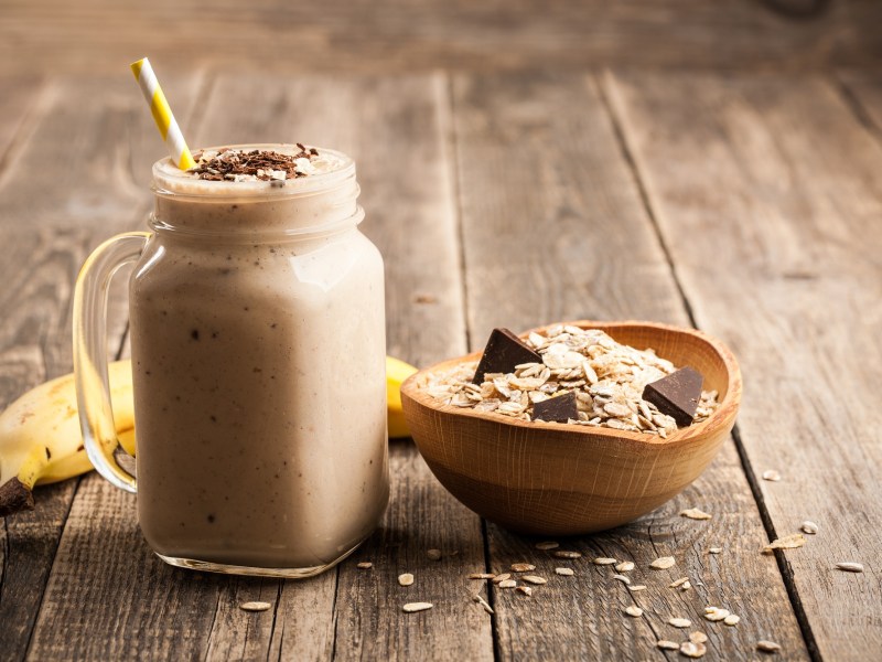 Glass with banana chocolate smoothie, bowl of oatmeal next to it