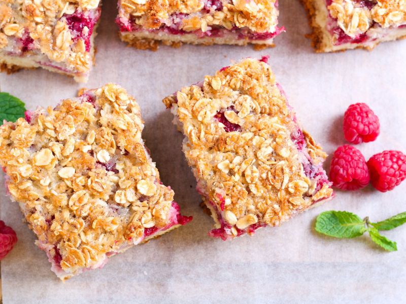No-sugar-added banana-raspberry bars on parchment paper, some raspberries lying next to it as decoration.