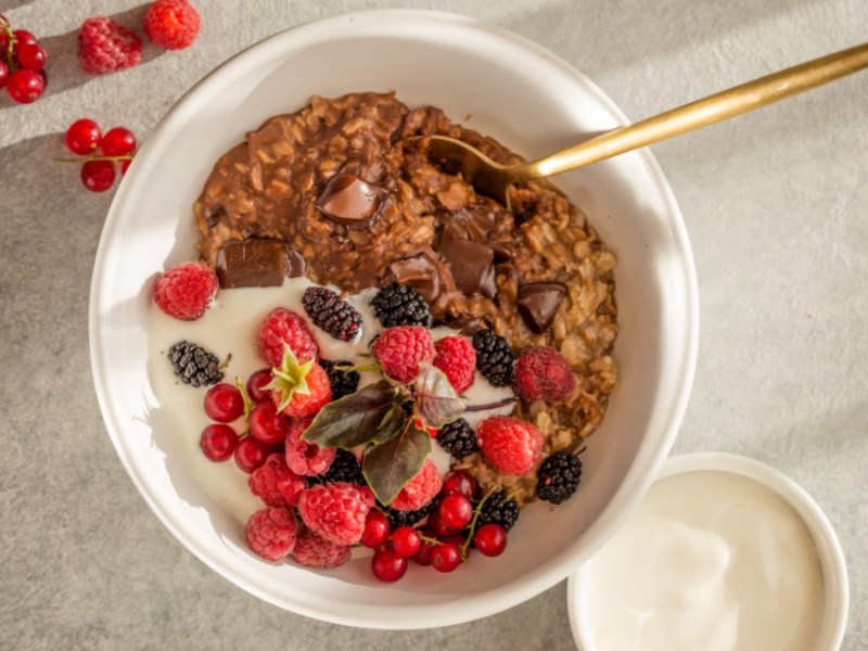 Chocolate oatmeal in a white bowl with fruit, top view.