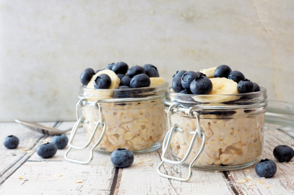 2 glasses of overnight oats garnished with blueberries and banana slices, with some blueberries scattered around.