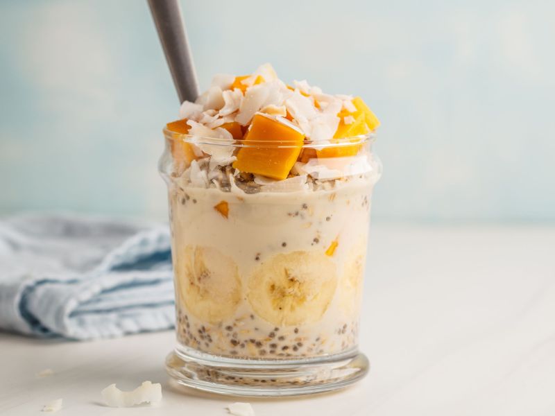 Mango Coconut Overnight Oats layered in a glass and served with a straw.