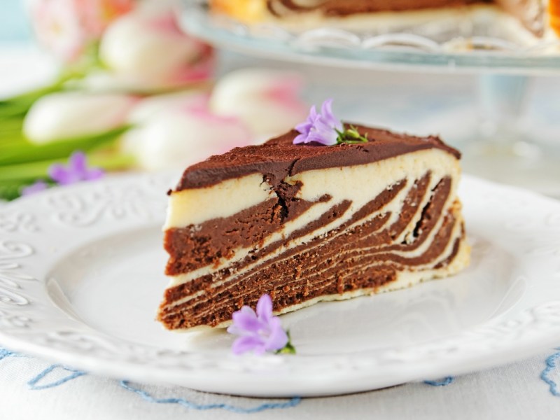 A slice of zebra cheesecake with light and dark batter on a plate, decorated with flowers.