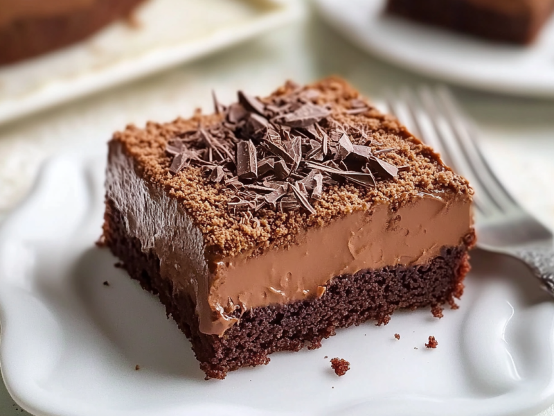 A piece of chocolate pudding sheet cake on a white plate. A fork lies next to it.