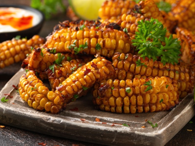A stack of corn ribs with parsley on a plate. Next to it is a bowl of dip.