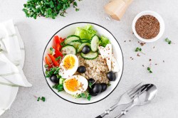 An oatmeal bowl with feta and egg, with bell peppers, lettuce, cucumbers, and olives.