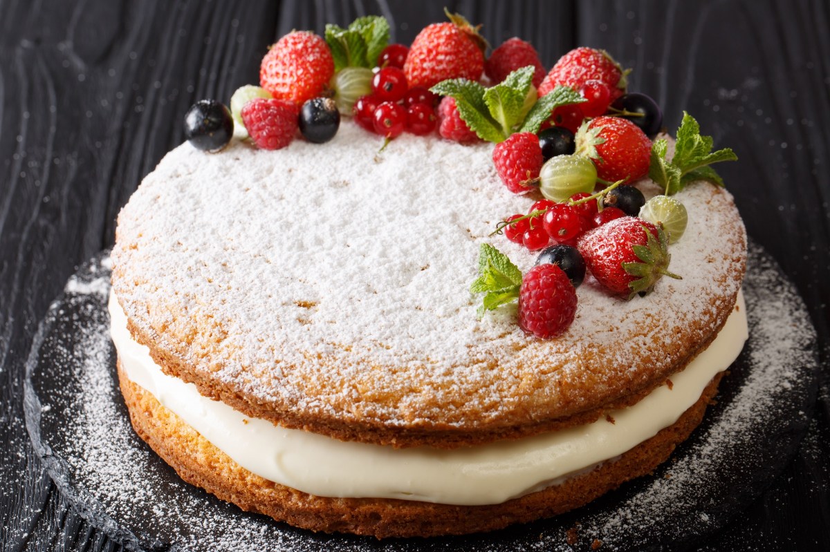 A Victoria Sponge Cake layered with cream, dusted with powdered sugar, and garnished with fresh berries.